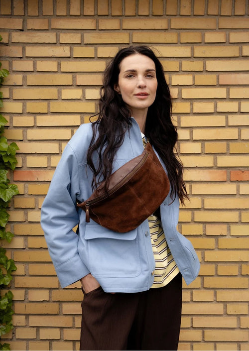 Bauchtasche Selma von Re:Designed in Woodsmoke aus weichem Veloursleder mit verstellbarem Crossbody-Gurt und Reißverschluss.