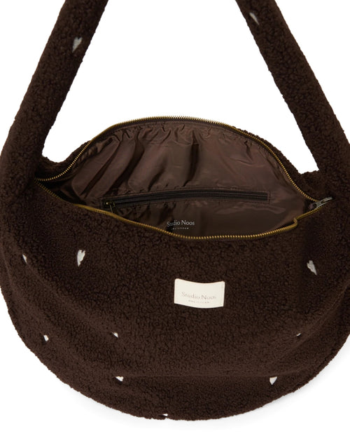 Schokoladenbraune Cross Body Umhängetasche Chocolate Teddy Hearts von Studio Noos aus weichem Teddy-Material und aufgestickten weißen Herzen mit Seitentaschen und Platz für einen 13-Zoll-Laptop.