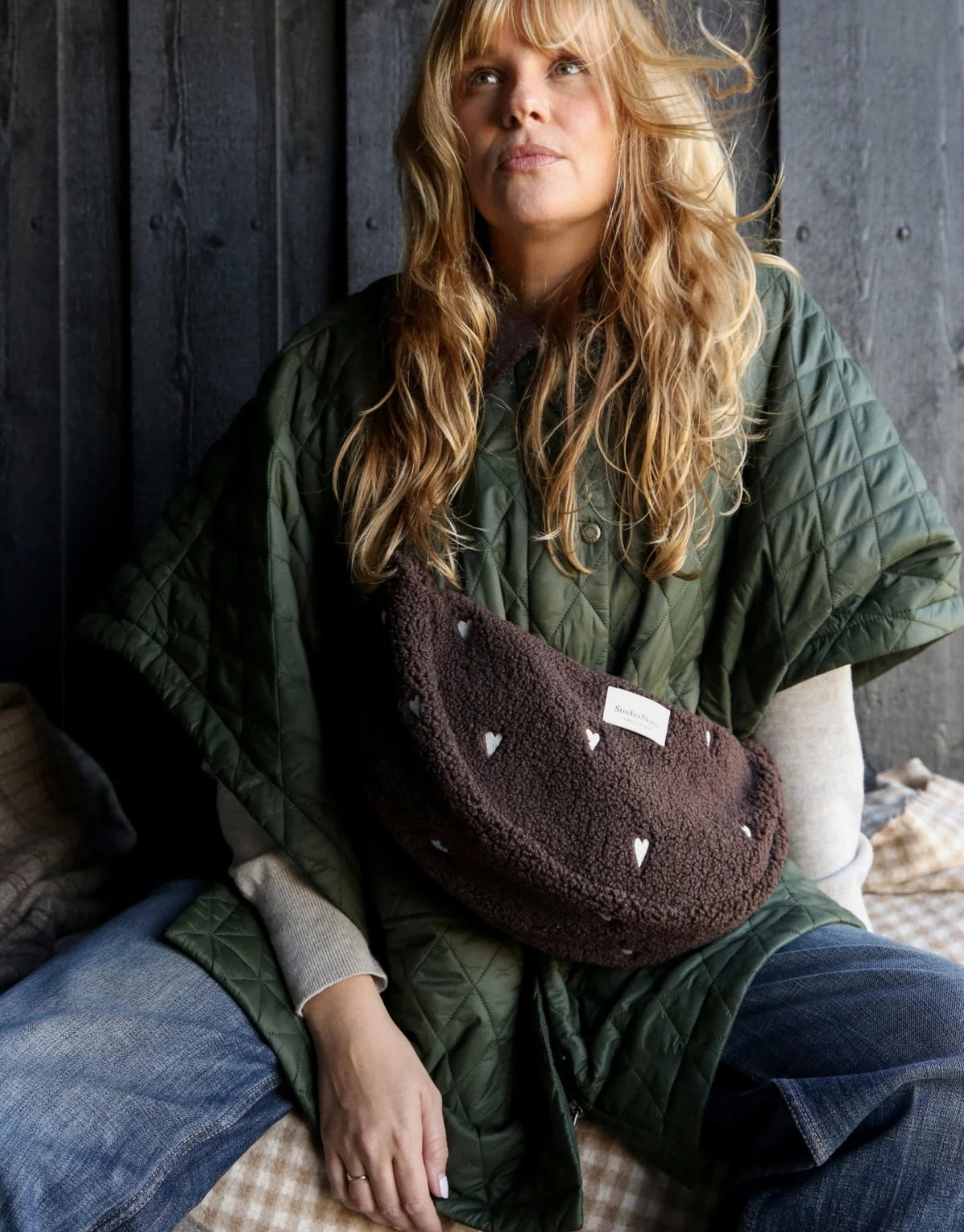 Schokoladenbraunes Fanny Pack Chocolate Teddy Hearts von Studio Noos aus weichem Teddy-Material mit gestickten Herzen und verstellbarem Riemen am Model.