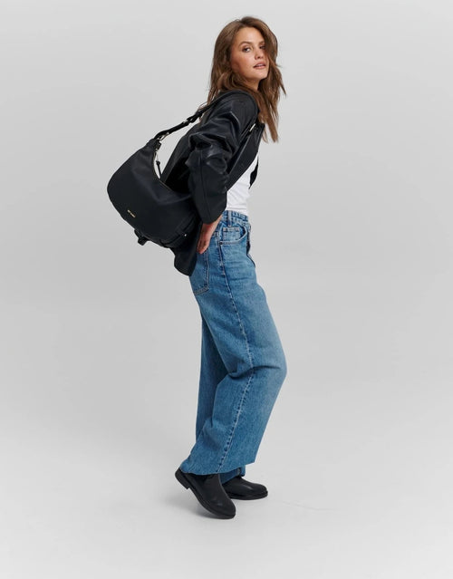 Schwarze Hey Marly Lifetime Sister M Umhängetasche mit flexibler Banana-Bag-Form, matt-goldfarbenen Details und verstellbarem Crossbody Strap am Model 