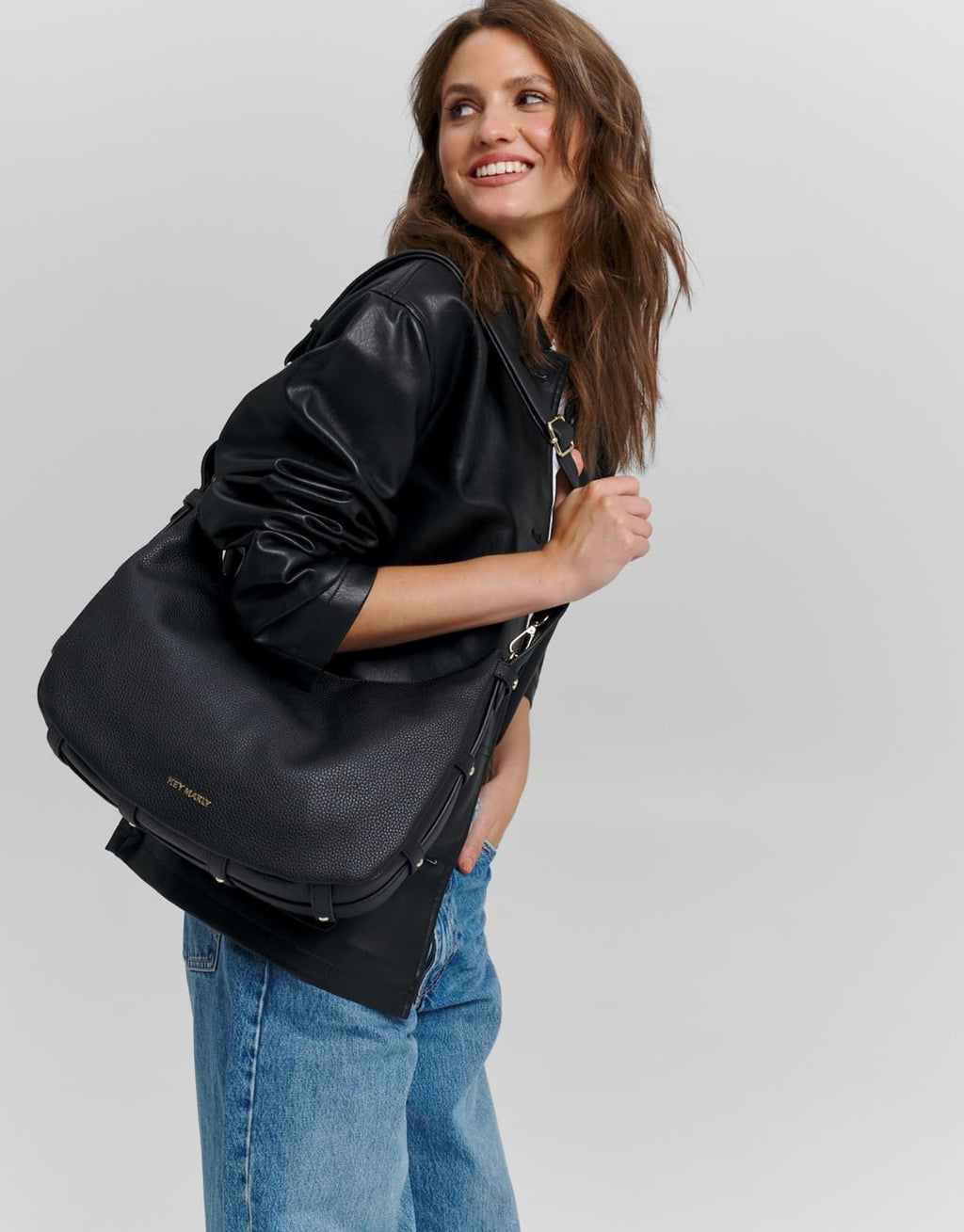 Schwarze Hey Marly Lifetime Sister M Umhängetasche mit flexibler Banana-Bag-Form, matt-goldfarbenen Details und verstellbarem Crossbody Strap am Model von der Seite 