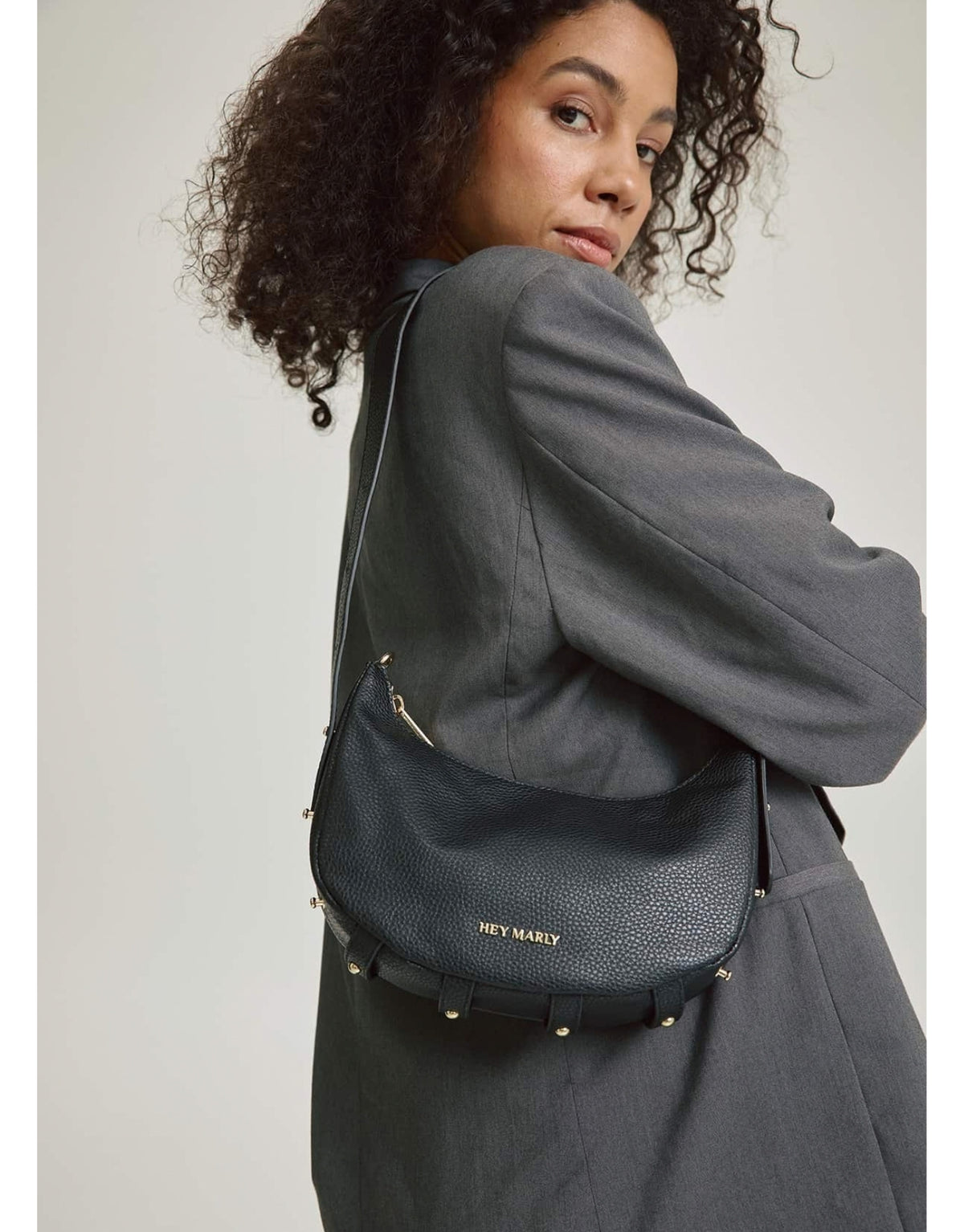 Schwarze Hey Marly Lifetime Sister S Umhängetasche in kompakter Banana-Bag-Form mit goldfarbenen Details und verstellbarem Schultergurt am Model von der Seite