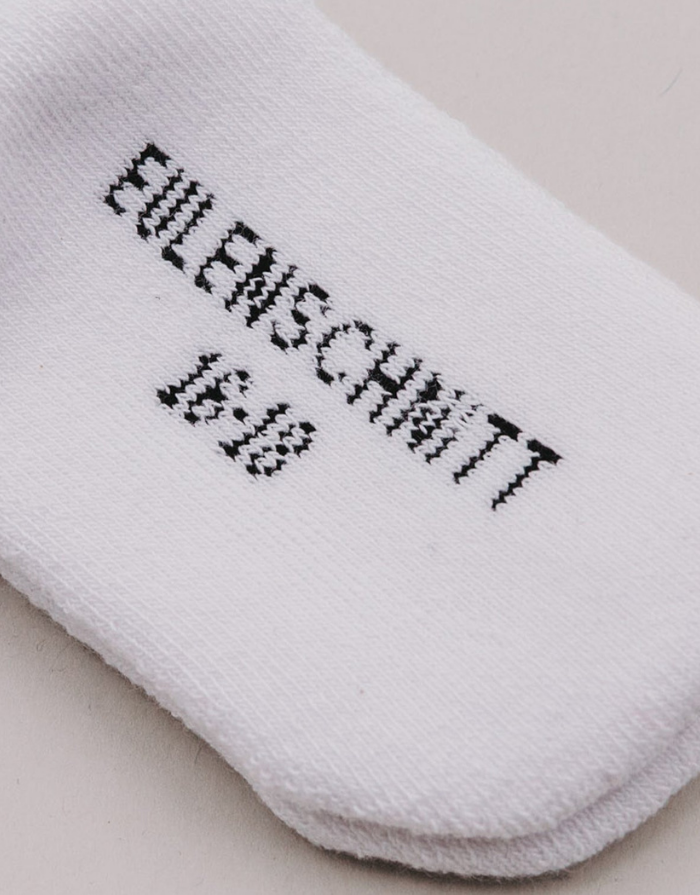 Weiße Babysocken Mini von Eulenschnitt mit schwarzem Schriftzug für Babys im Alter von 3 Monaten