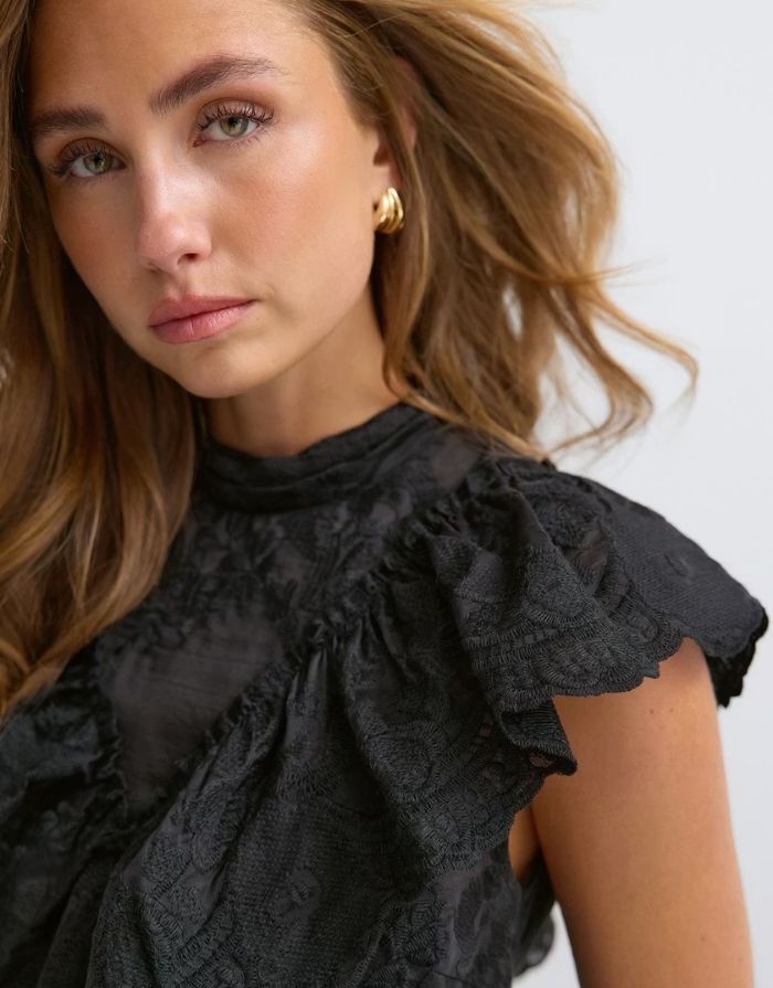 Schwarze ärmellose Frill Bluse von Gina Tricot mit hohem Kragen, Rüschen, Stickereien und figurbetonter Passform am Model im Detail
