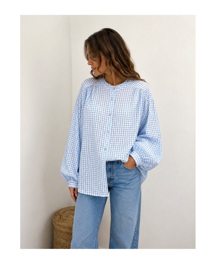 Bluse Karo Light Blue von MAËLYS PARIS mit Vichy-Karomuster, Rundhalsausschnitt und langen Ärmeln mit geknöpften Manschetten.