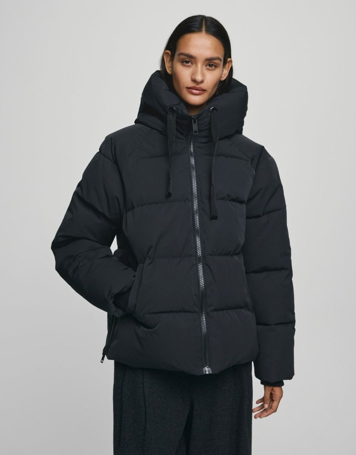 Schwarze kurze Winterjacke Pavinaria Short von MSCH Copenhagen mit Kapuze, hohem Kragen, leichter Wattierung und seitlichen Reißverschlüssen.