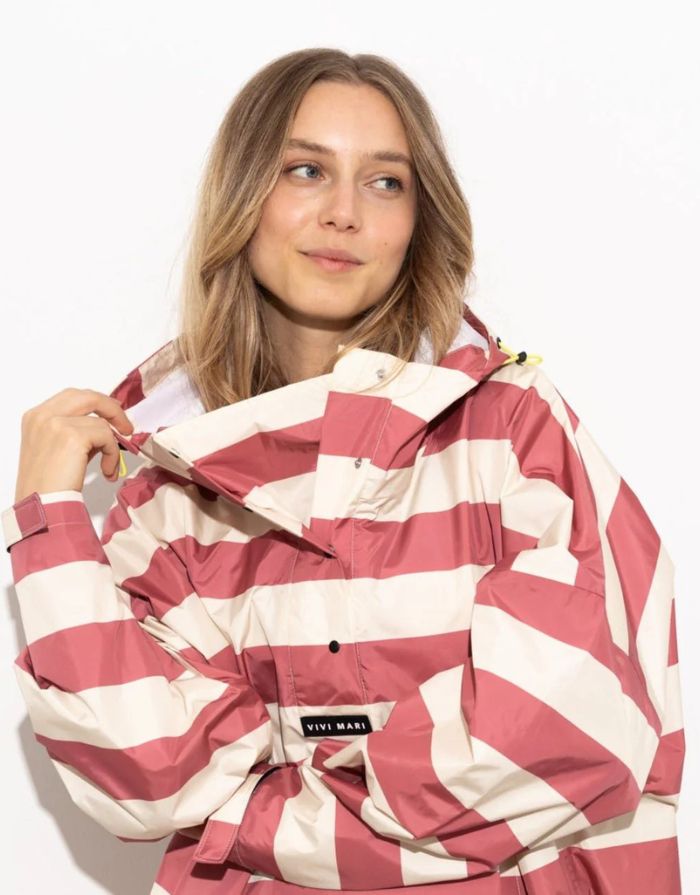 Raincoat Bold Stripes Blush/Sand von VIVI MARI: Langer, wasserdichter Regenmantel im Streifen-Design, oversized geschnitten mit Kapuze, Knopfleiste, Klettverschluss-Manschetten und praktischen Taschen – nachhaltig aus recyceltem Polyester gefertigt.