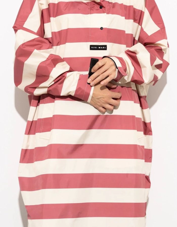 Raincoat Bold Stripes Blush/Sand von VIVI MARI: Langer, wasserdichter Regenmantel im Streifen-Design, oversized geschnitten mit Kapuze, Knopfleiste, Klettverschluss-Manschetten und praktischen Taschen – nachhaltig aus recyceltem Polyester gefertigt.