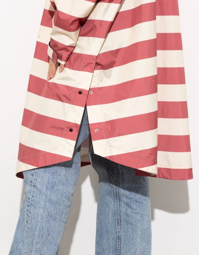 Raincoat Bold Stripes Blush/Sand von VIVI MARI: Langer, wasserdichter Regenmantel im Streifen-Design, oversized geschnitten mit Kapuze, Knopfleiste, Klettverschluss-Manschetten und praktischen Taschen – nachhaltig aus recyceltem Polyester gefertigt.