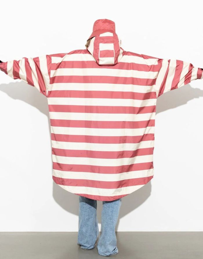 Raincoat Bold Stripes Blush/Sand von VIVI MARI: Langer, wasserdichter Regenmantel im Streifen-Design, oversized geschnitten mit Kapuze, Knopfleiste, Klettverschluss-Manschetten und praktischen Taschen – nachhaltig aus recyceltem Polyester gefertigt.