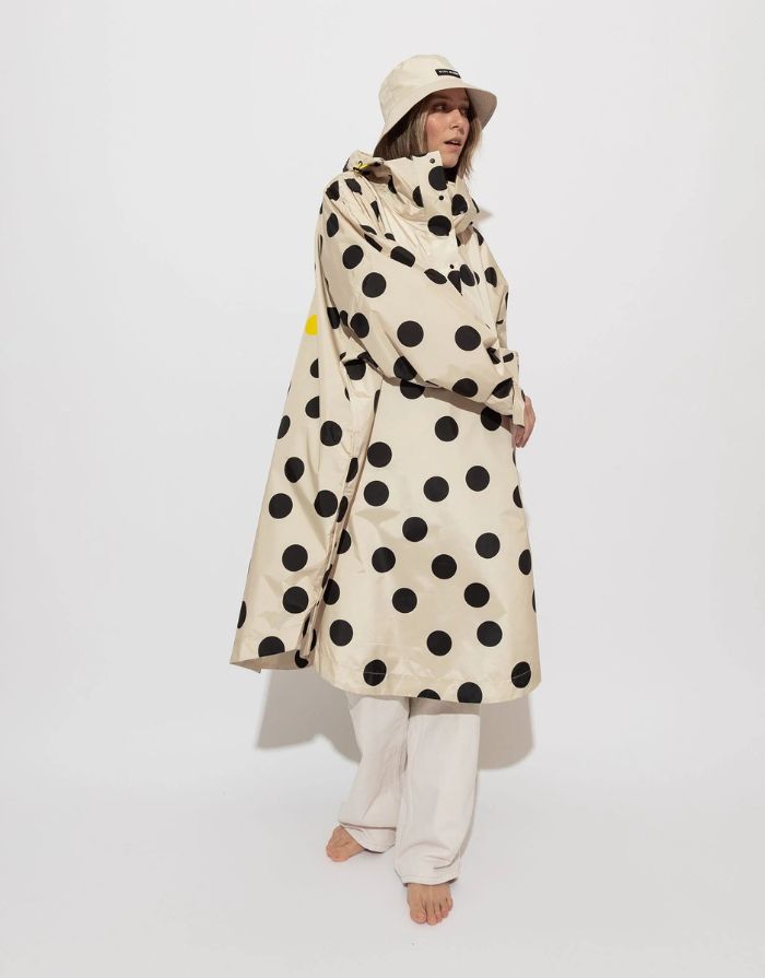 Raincoat Bold Stripes Dots Black/Sand von VIVI MARI: Langer, wasserdichter Regenmantel im Streifen-Design, oversized geschnitten mit Kapuze, Knopfleiste, Klettverschluss-Manschetten und praktischen Taschen – nachhaltig aus recyceltem Polyester gefertigt.