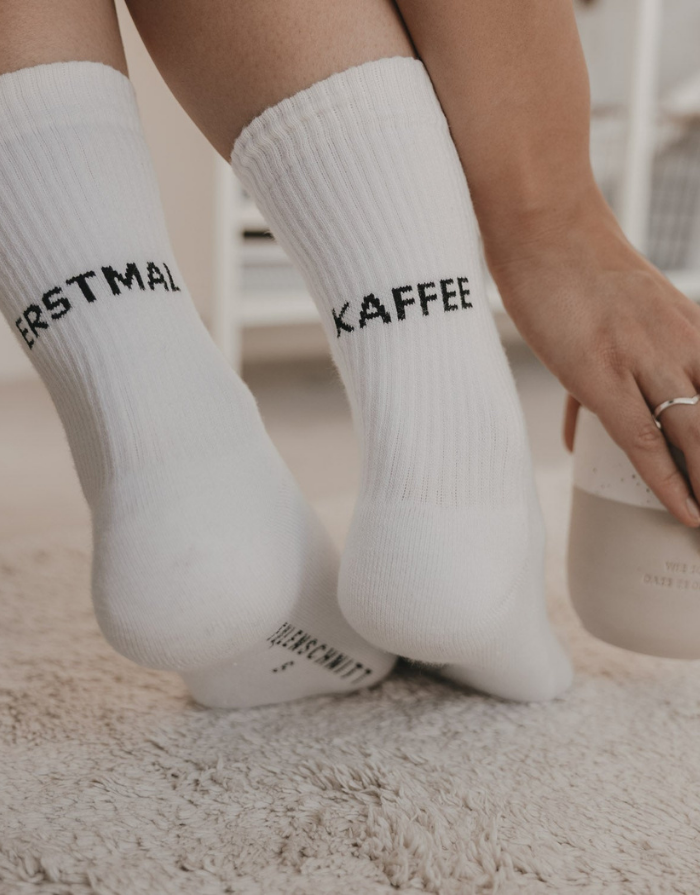 Weiße Socken Erstmal Kaffee von Eulenschnitt mit schwarzem Schriftzug an der Ferse und schwarzen Details