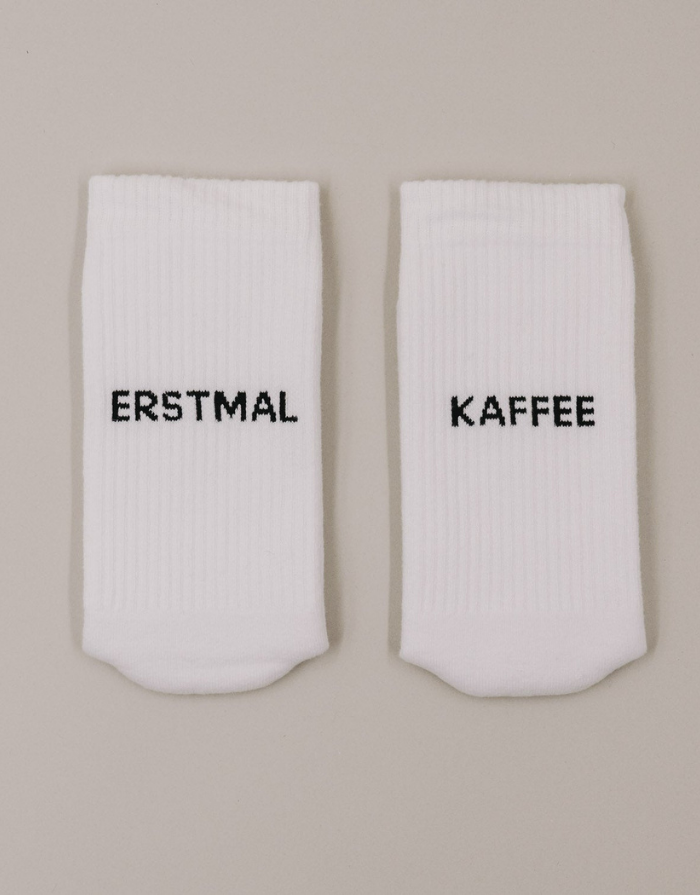 Weiße Socken Erstmal Kaffee von Eulenschnitt mit schwarzem Schriftzug an der Ferse und schwarzen Details