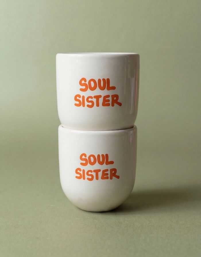 Becher Soul Sister von Sisi House of Style in Weiß mit orangefarbenem Soul Sister Schriftzug mit einem weiteren Becher darauf gestapelt
