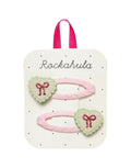 Sweet Heart Bow Haarspangen von Rockahula mit Herzmotiven, glitzernden roten Schleifen und rosafarbenen, stoffbezogenen Klickspangen.