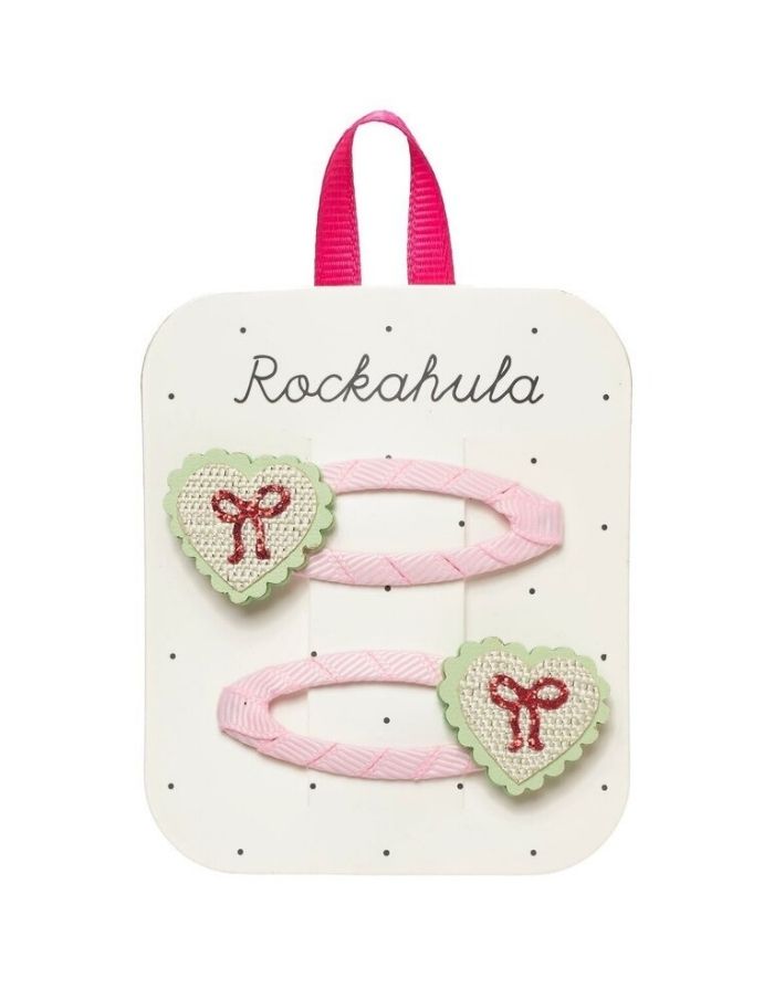 Sweet Heart Bow Haarspangen von Rockahula mit Herzmotiven, glitzernden roten Schleifen und rosafarbenen, stoffbezogenen Klickspangen.