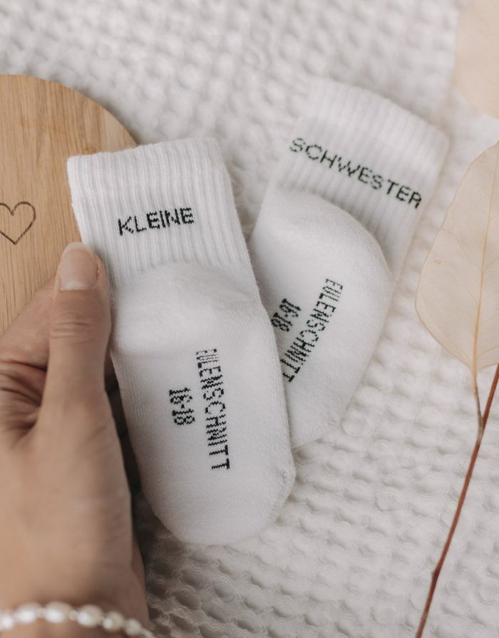 Babysocken Kleine Schwester von Eulenschnitt, 80% Baumwolle, 18% Polyamid, 2% Elastan, mit Schriftzug „Kleine Schwester“ auf dem Bündchen.