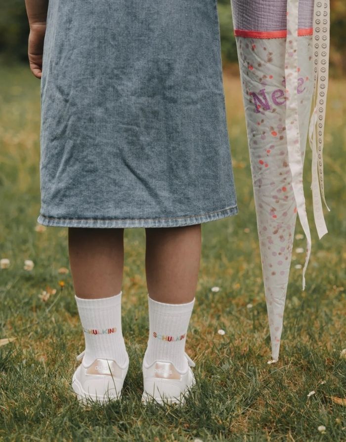 Weiße Eulenschnitt Socken „Schulkind“ mit buntem Schriftzug auf der Ferse und weichen Bündchen für Kinder an einem Kind von hinten