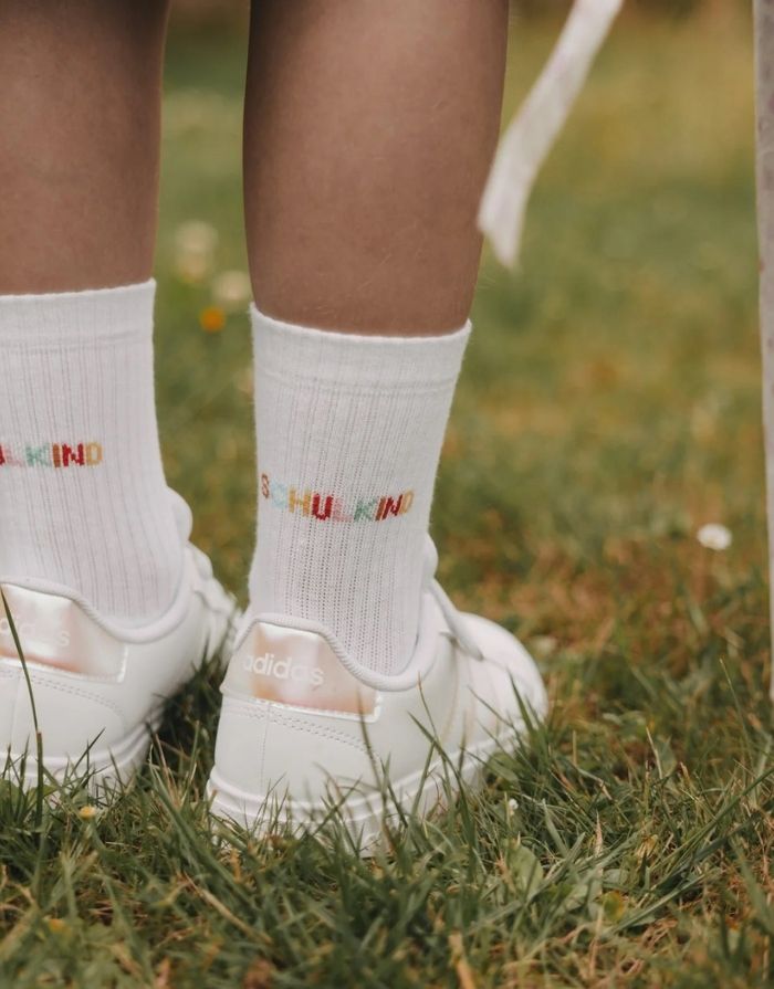 Weiße Eulenschnitt Socken „Schulkind“ mit buntem Schriftzug auf der Ferse und weichen Bündchen für Kinder an einem Kind im Detail