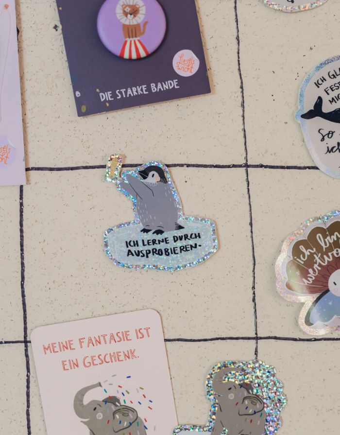 Glitzersticker von Liesels Wicht mit liebevollem Motiv und motivierender Botschaft für Kinder auf glänzendem Glitzervinyl vor einer Wand.