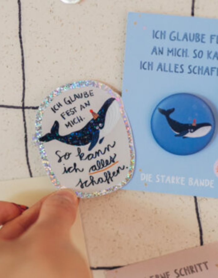 Glitzersticker Wal von Liesels Wicht mit liebevollem Motiv und motivierender Botschaft für Kinder auf glänzendem Glitzervinylvor einer Wand.