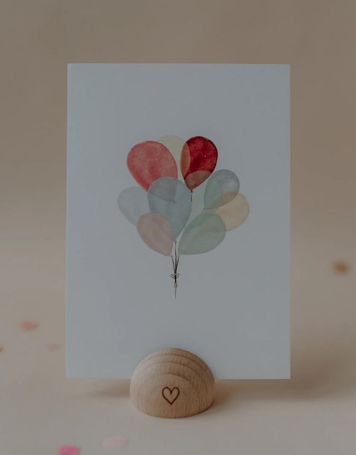 Postkarte von Eulenschnitt in weiß mit bunten Luftballons in einem Kartenständer