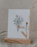 Postkarte von Eulenschnitt in einem Kartenständer mit einer Hand mit Blumenstrauß