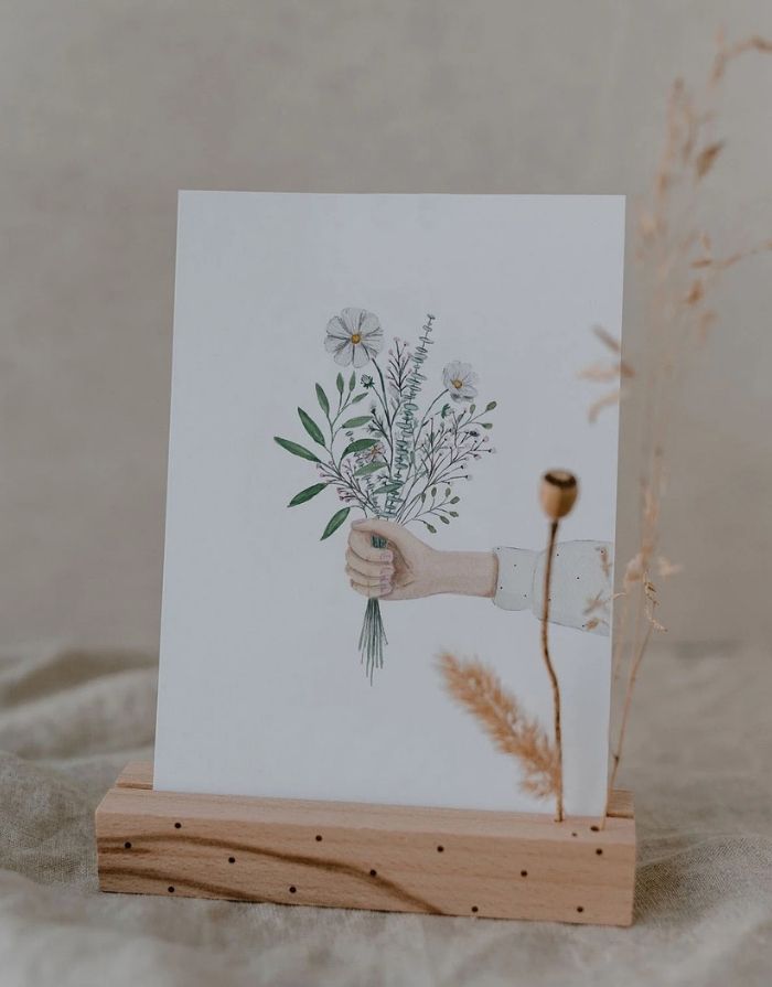 Postkarte von Eulenschnitt in einem Kartenständer mit einer Hand mit Blumenstrauß